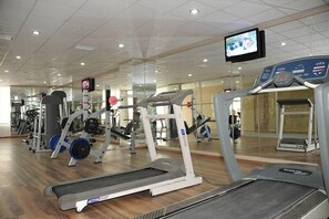 Un gimnàs amb cintes de córrer, aparells de musculació i una pantalla de televisió.