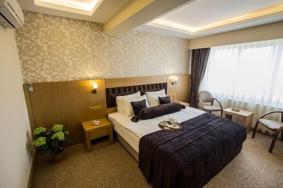 A hotel room with a large bed, bedside tables, a chair, and a potted plant.
