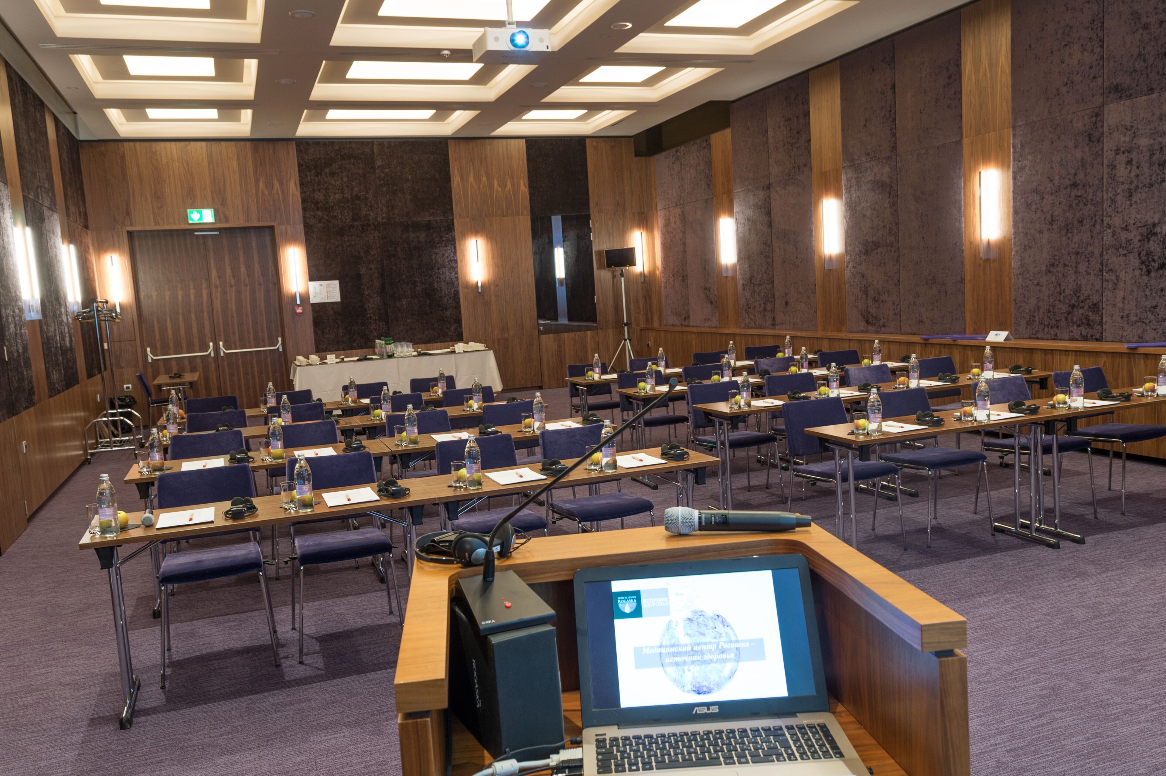 A conference room with rows of tables and chairs, equipped with laptops, microphones, and water bottles.