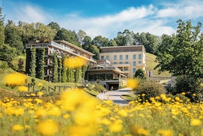 A modern building with a glass facade, surrounded by lush greenery and a field of yellow flowers. - Atlantida Boutique Hotel (Rogaska Slatina)