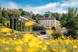Un edificio moderno con fachada de vidrio, rodeado de abundante vegetación y un campo de flores amarillas.