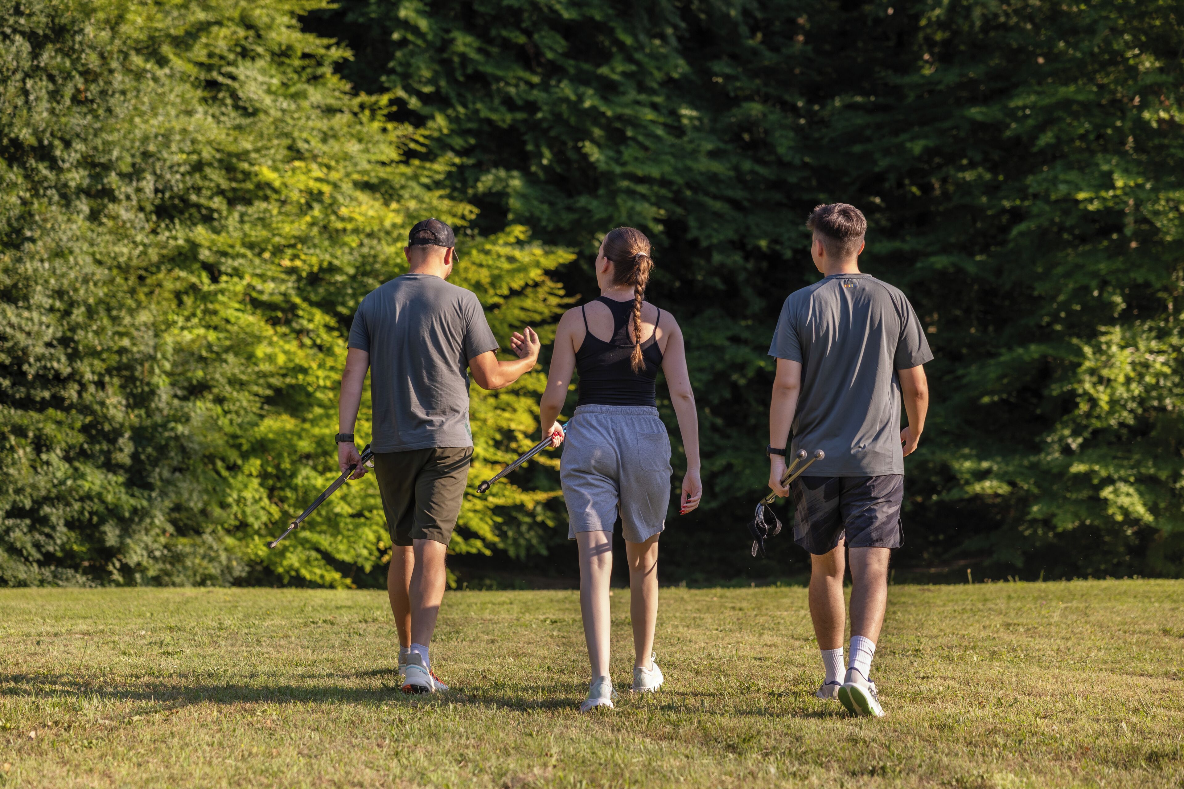 Tres personas caminando sobre un campo cubierto de césped, con árboles al fondo.