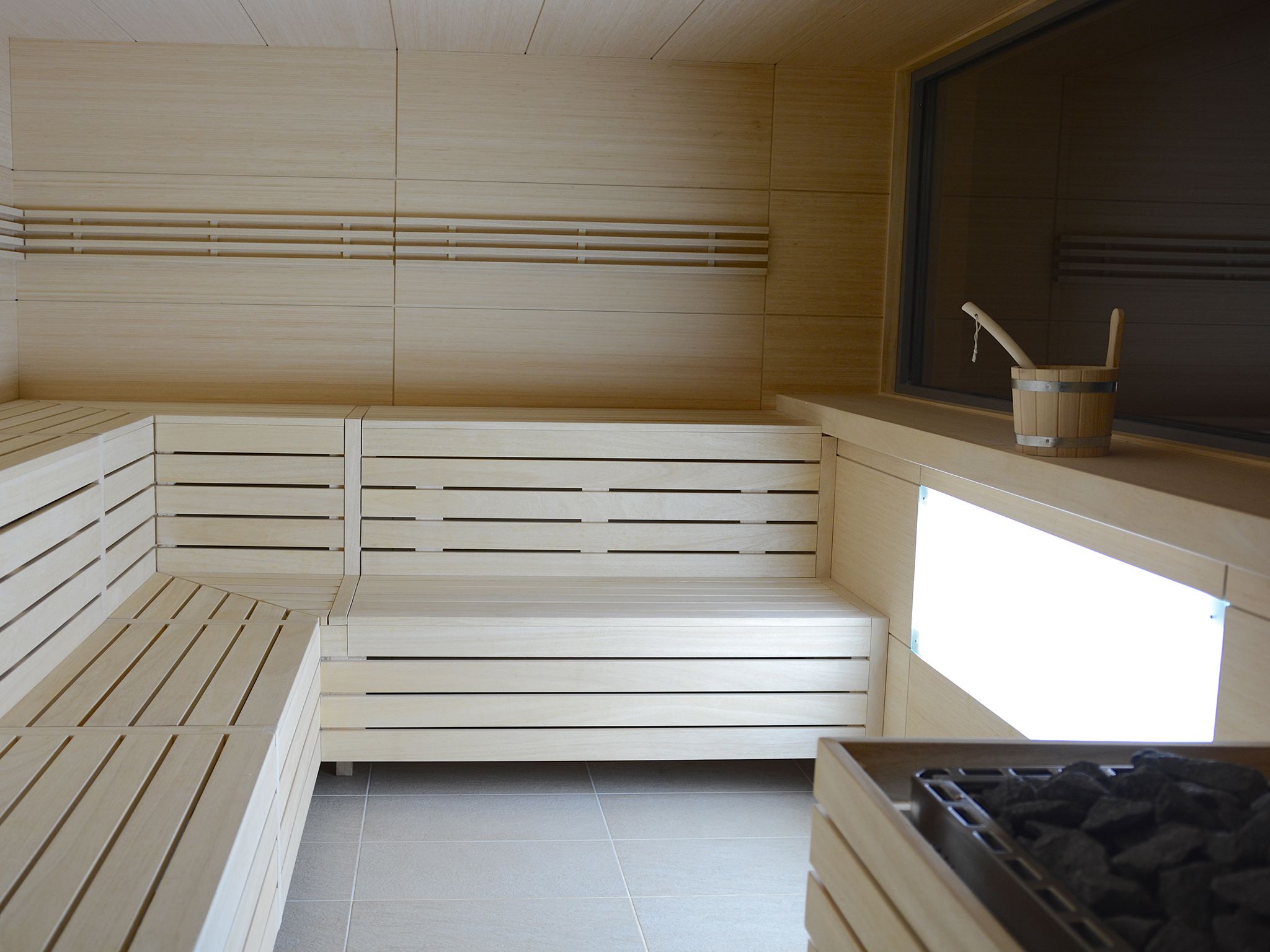Una sala de sauna con bancos de madera, una ventana y un cubo.