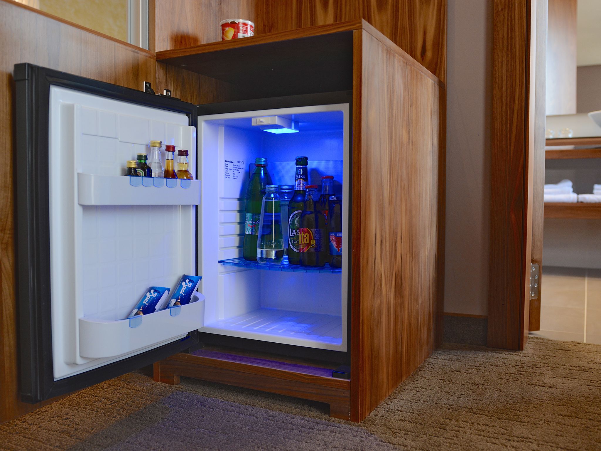 A compact refrigerator with a wooden exterior, containing various beverages and condiments.