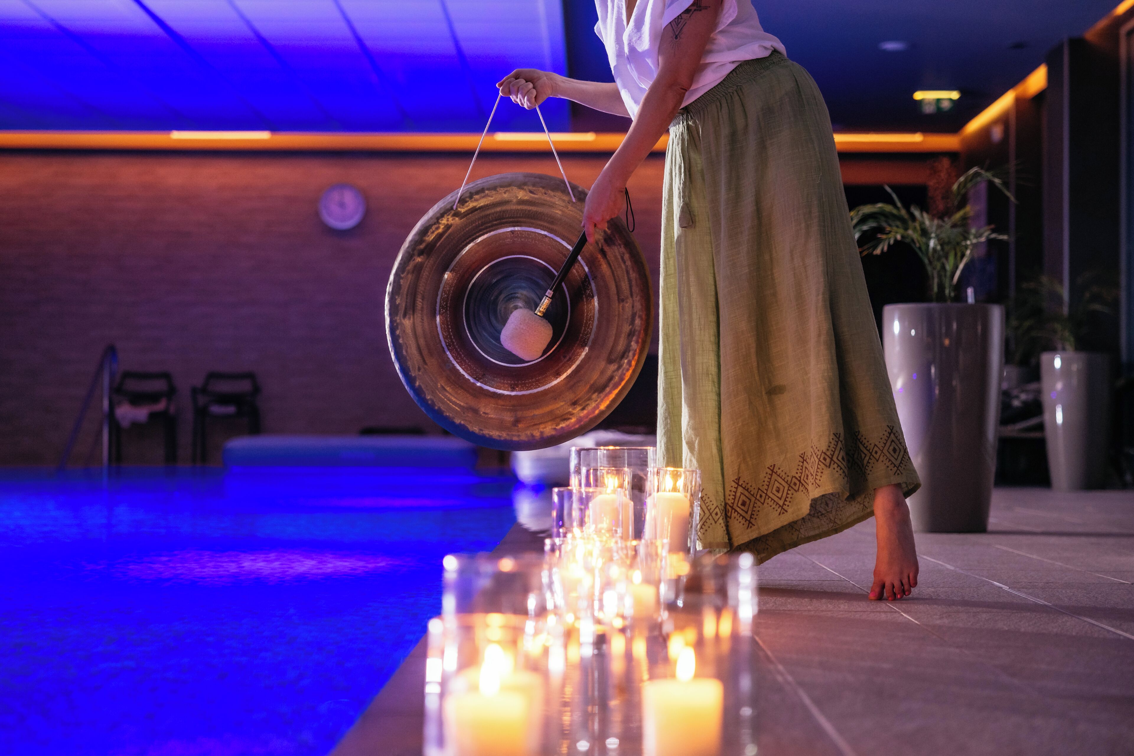 Una persona sostiene un objeto grande, redondo y reflectante, posiblemente un espejo o un adorno, en una habitación con suelo de baldosas y varias velas encendidas.