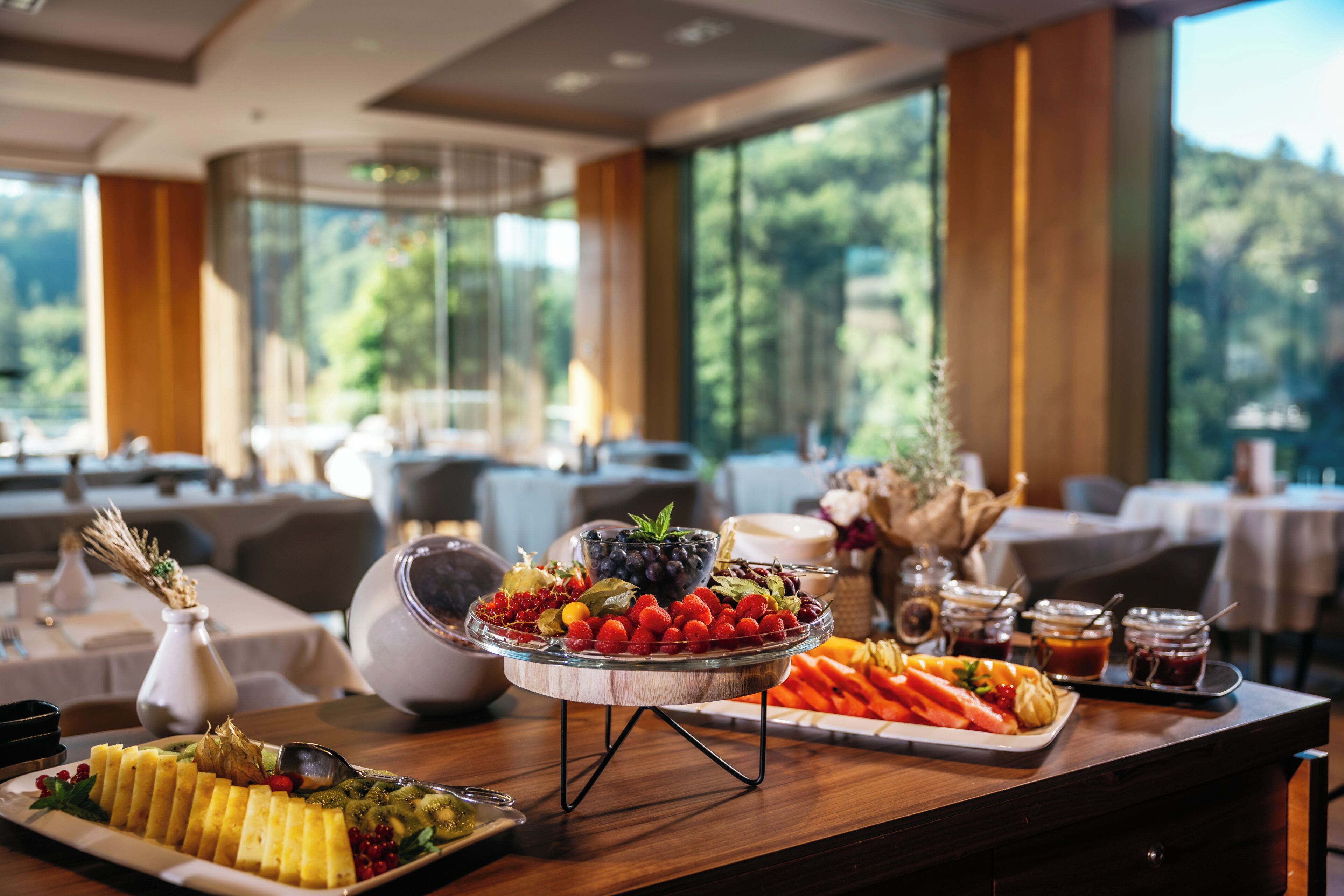 A buffet table with a variety of fruits and vegetables, a white vase with dried flowers, and a glass bowl with berries.