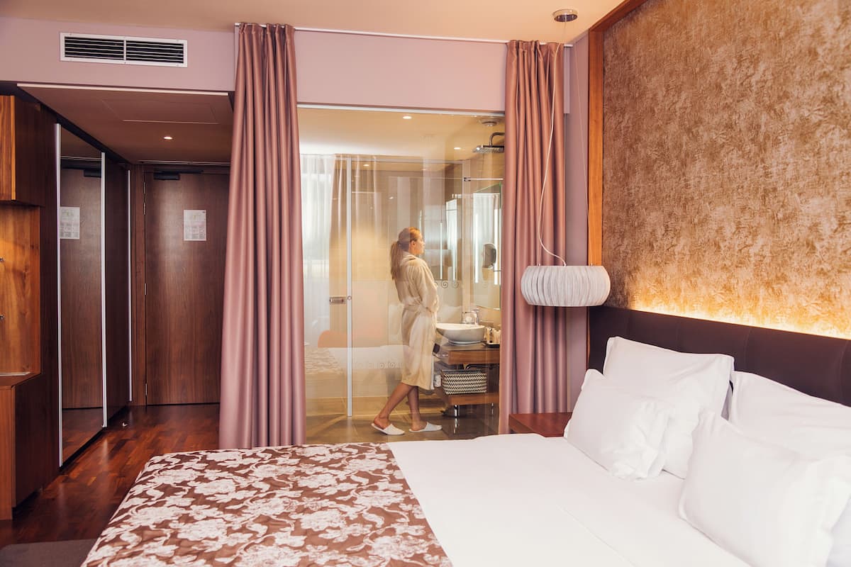 A hotel room with a large bed, a bathroom with a glass door, and wooden furniture.
