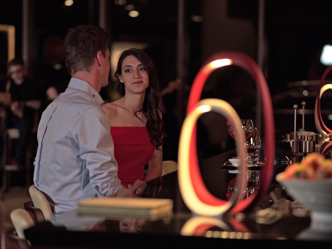 A couple seated at a table with a glass of wine, surrounded by a dimly lit restaurant interior.