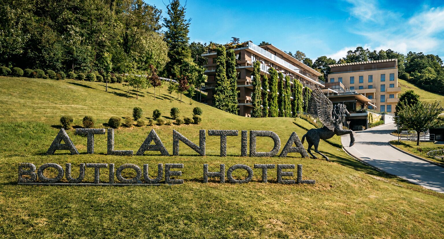 A sign for the Atlantida Boutique Hotel with a horse statue, surrounded by a well-manicured lawn and trees.