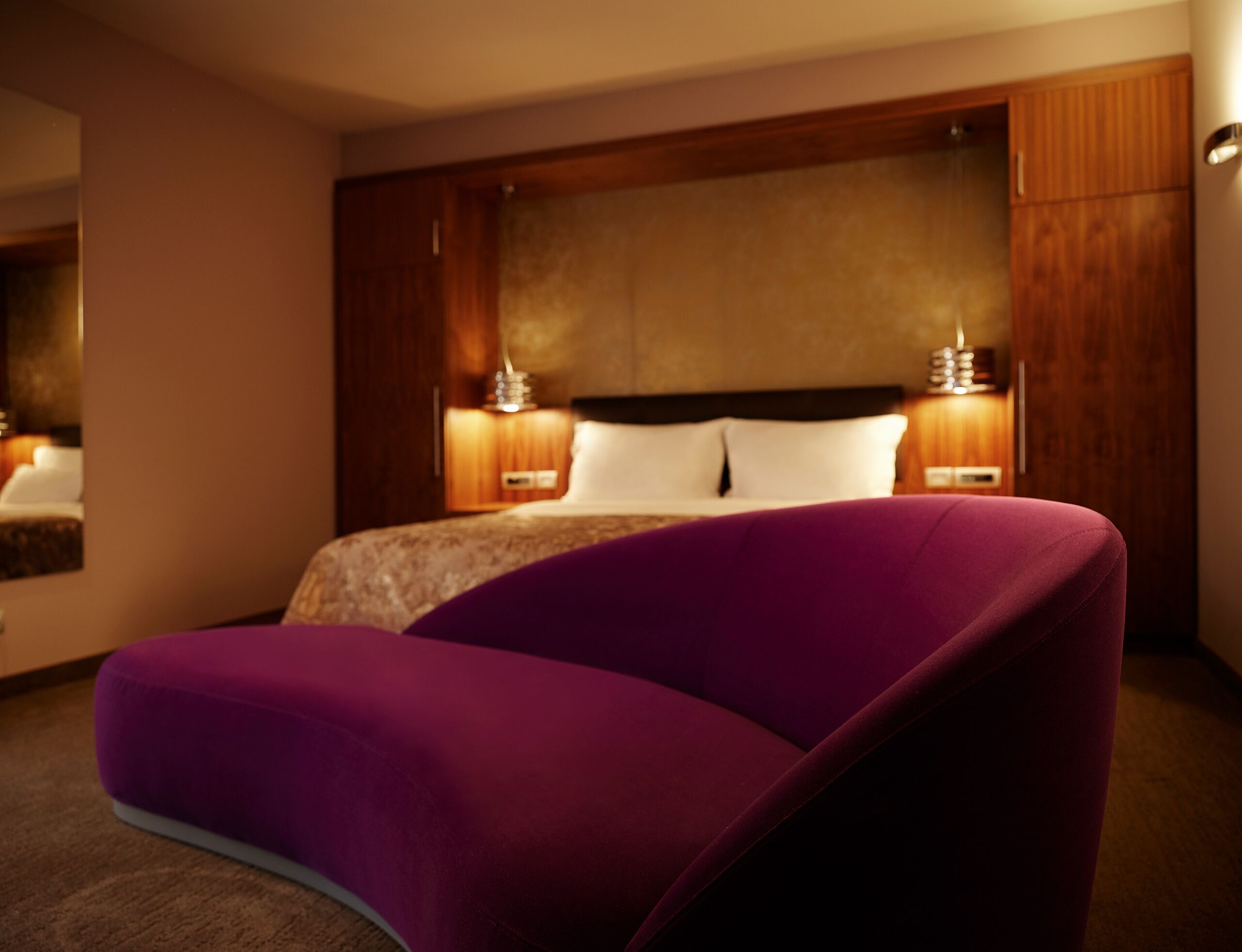 A modern hotel room with a large bed, a purple chair, and wooden paneling on the walls.