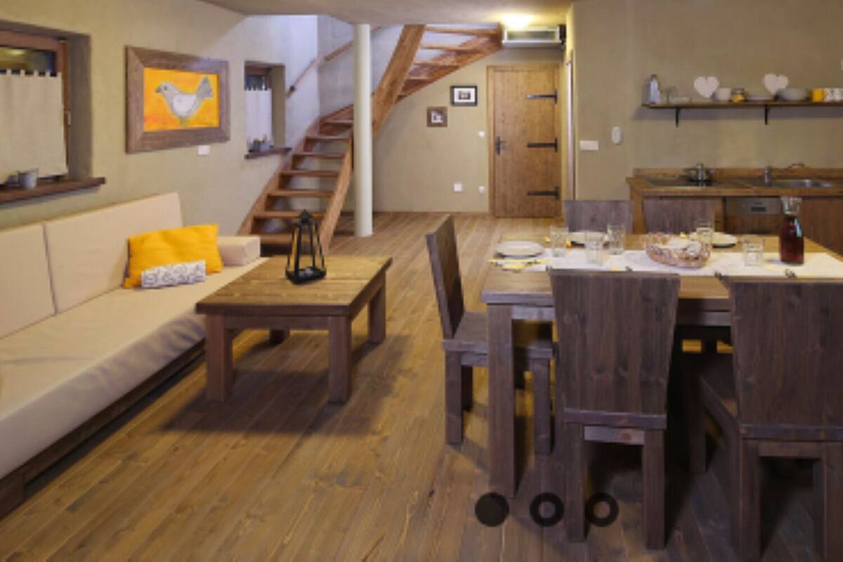 A cozy dining area with a wooden table and chairs, a staircase leading to another room, and a kitchen area with a microwave and shelves.
