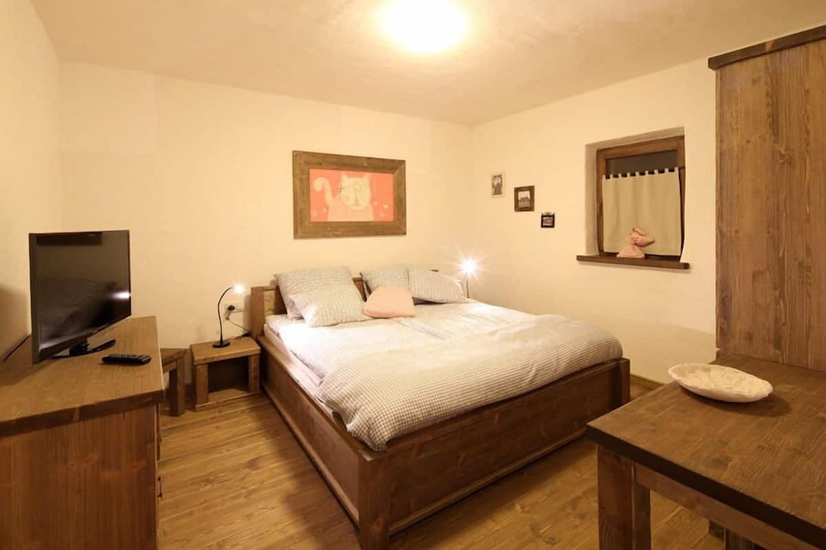 A bedroom with a wooden bed, bedside tables, a television, a window with curtains, and a framed picture on the wall.