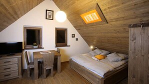 Un dormitorio acogedor en el ático con techo de madera, una cama, un escritorio y un televisor.