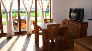 Una mesa de comedor de madera con sillas, un televisor sobre un mueble de madera y ventanas grandes con cortinas.