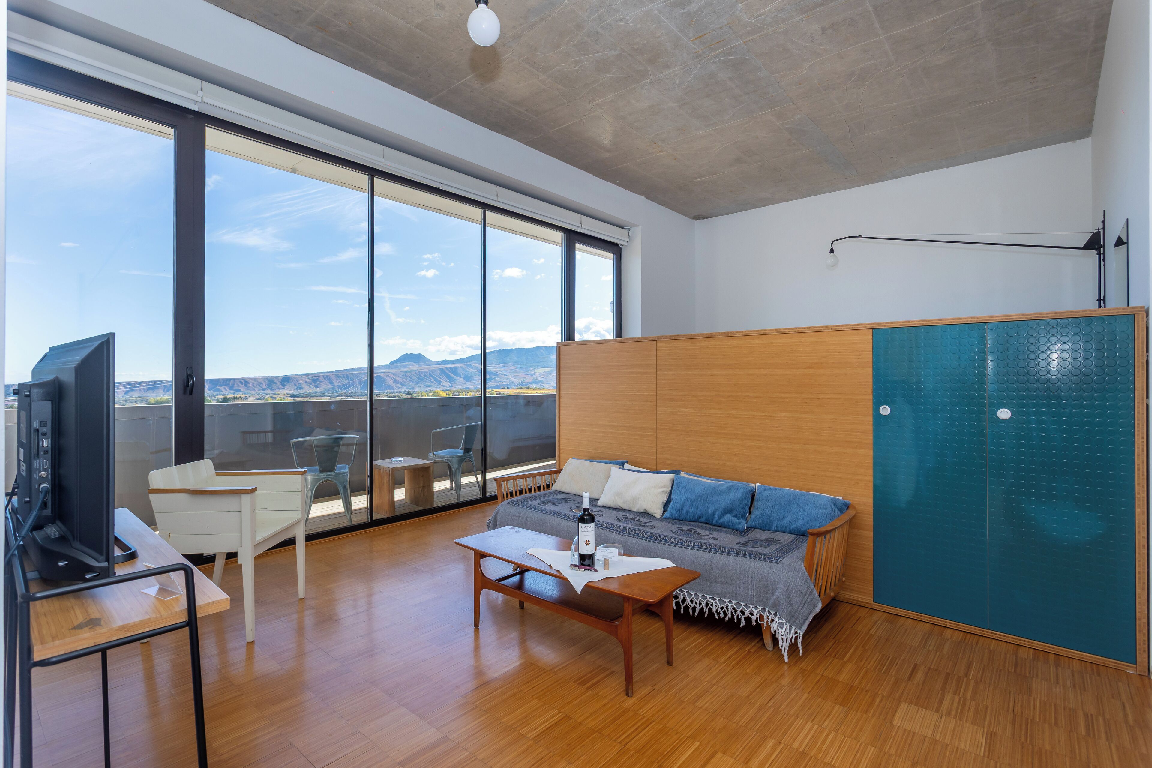 A modern room with a large sliding glass door, a wooden desk, a sofa, and a TV.