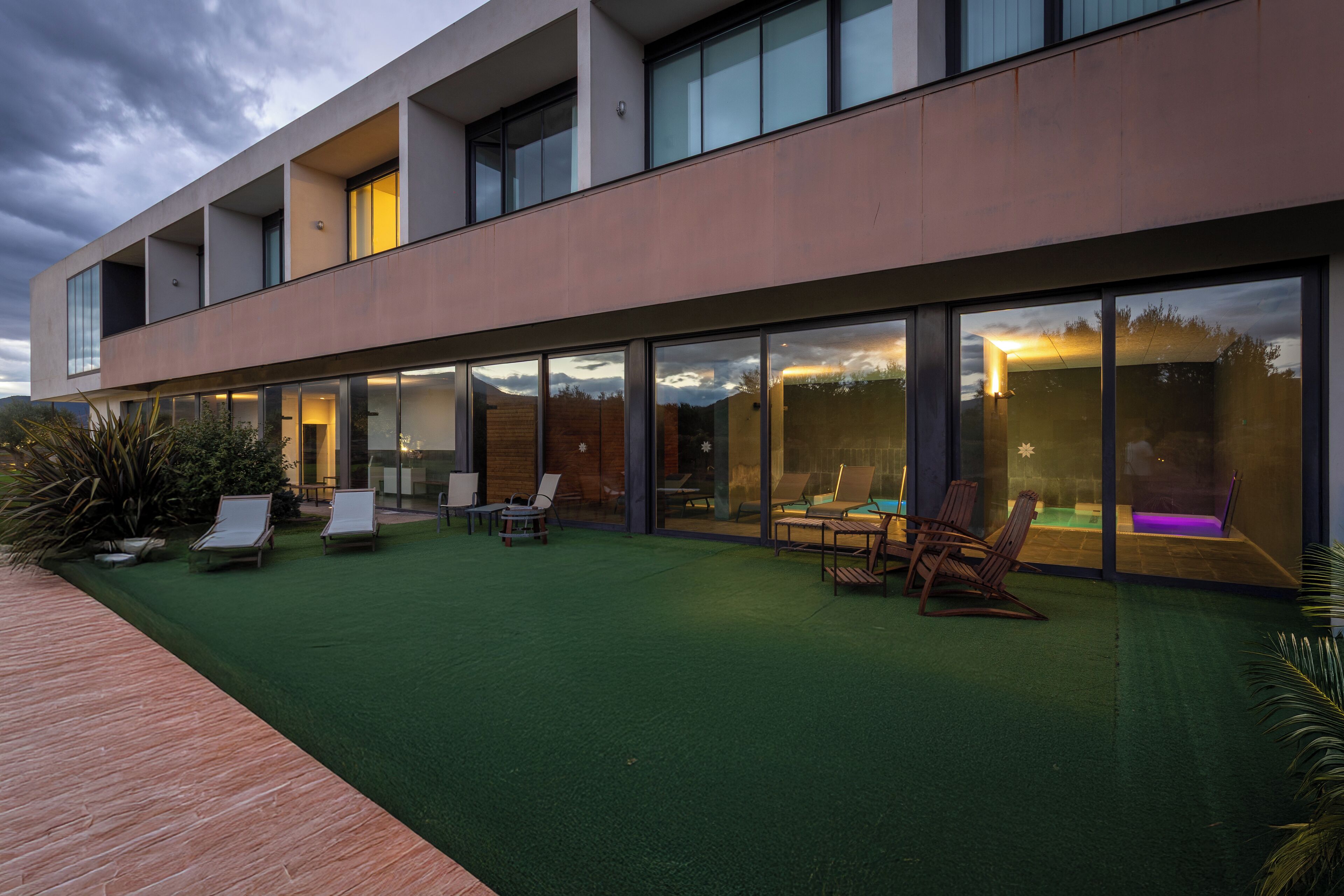 Un edificio moderno con techo plano, ventanas amplias y un patio con mobiliario exterior.