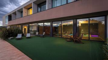 Un edificio moderno con techo plano, ventanas amplias y un patio con mobiliario exterior.