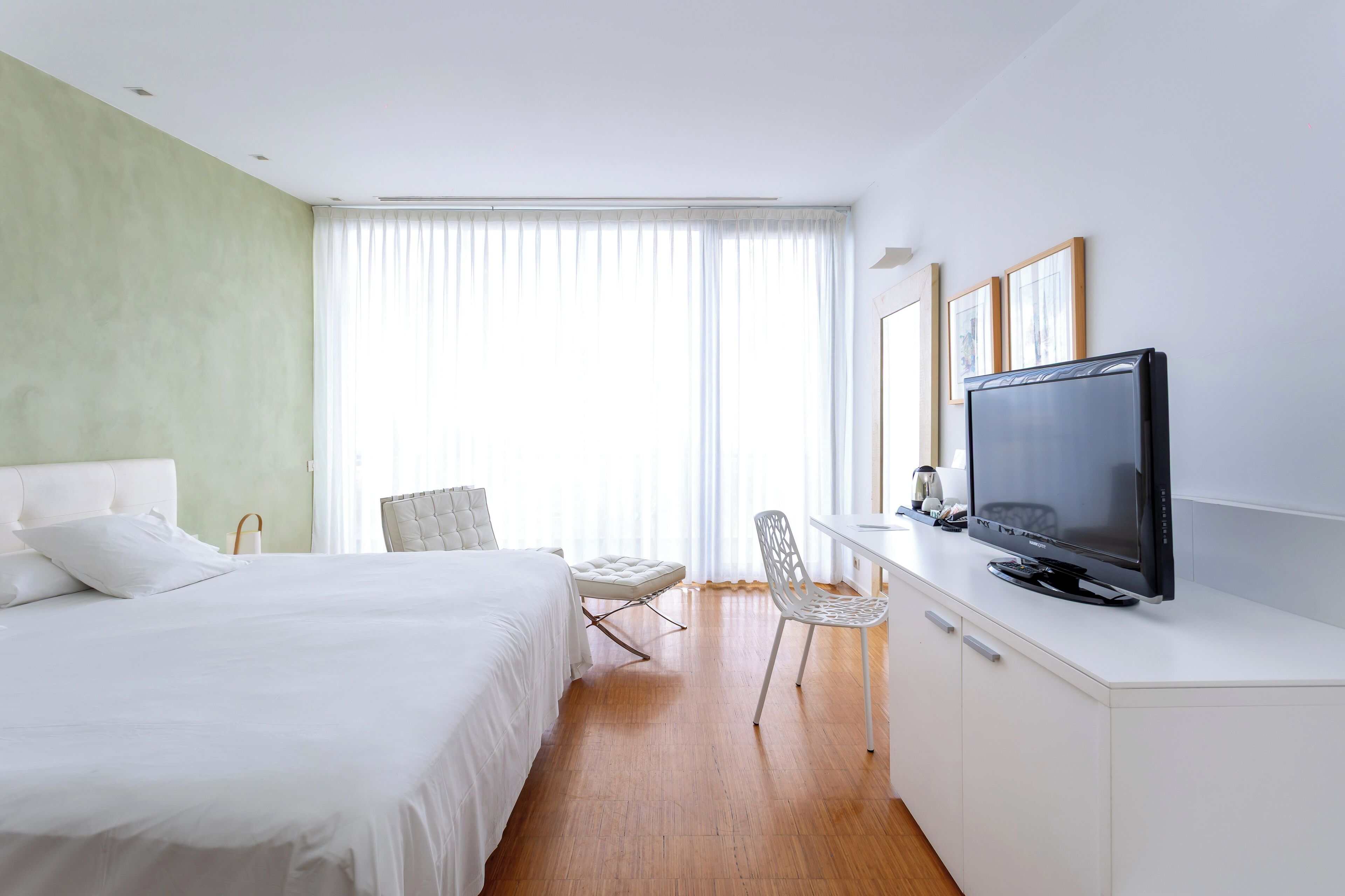 A hotel room with a bed, a desk with a television, a chair, and a window with curtains.