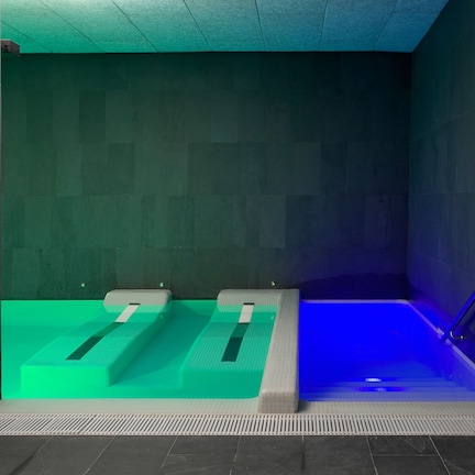 A modern spa room with two separate soaking tubs, one illuminated with blue light.