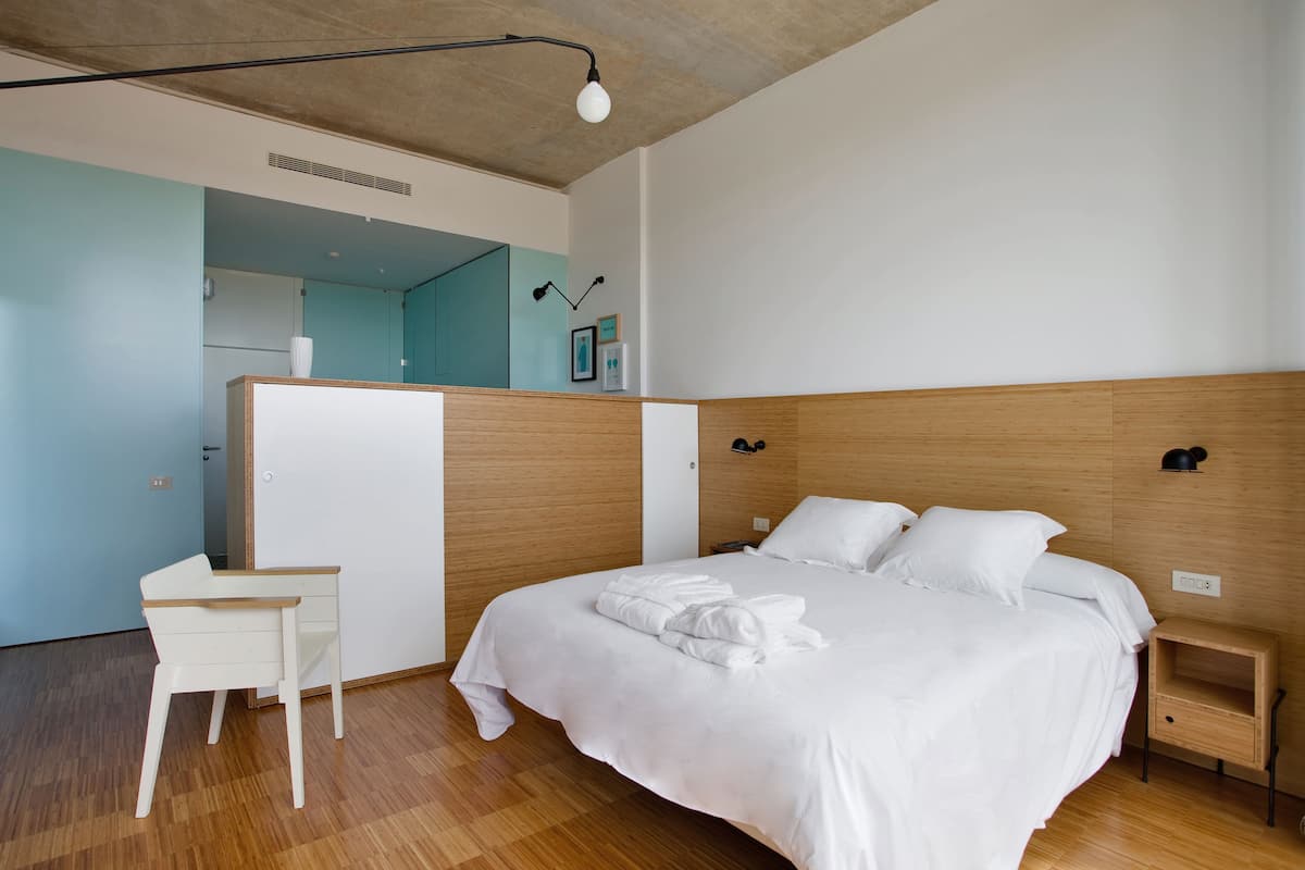 Una habitación de hotel moderna con cabecera de madera, una cama bien hecha, un escritorio pequeño y un espejo.