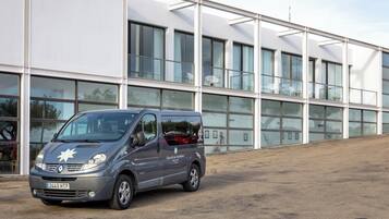 Una camioneta gris estacionada frente a un edificio moderno con ventanas grandes y techo plano.