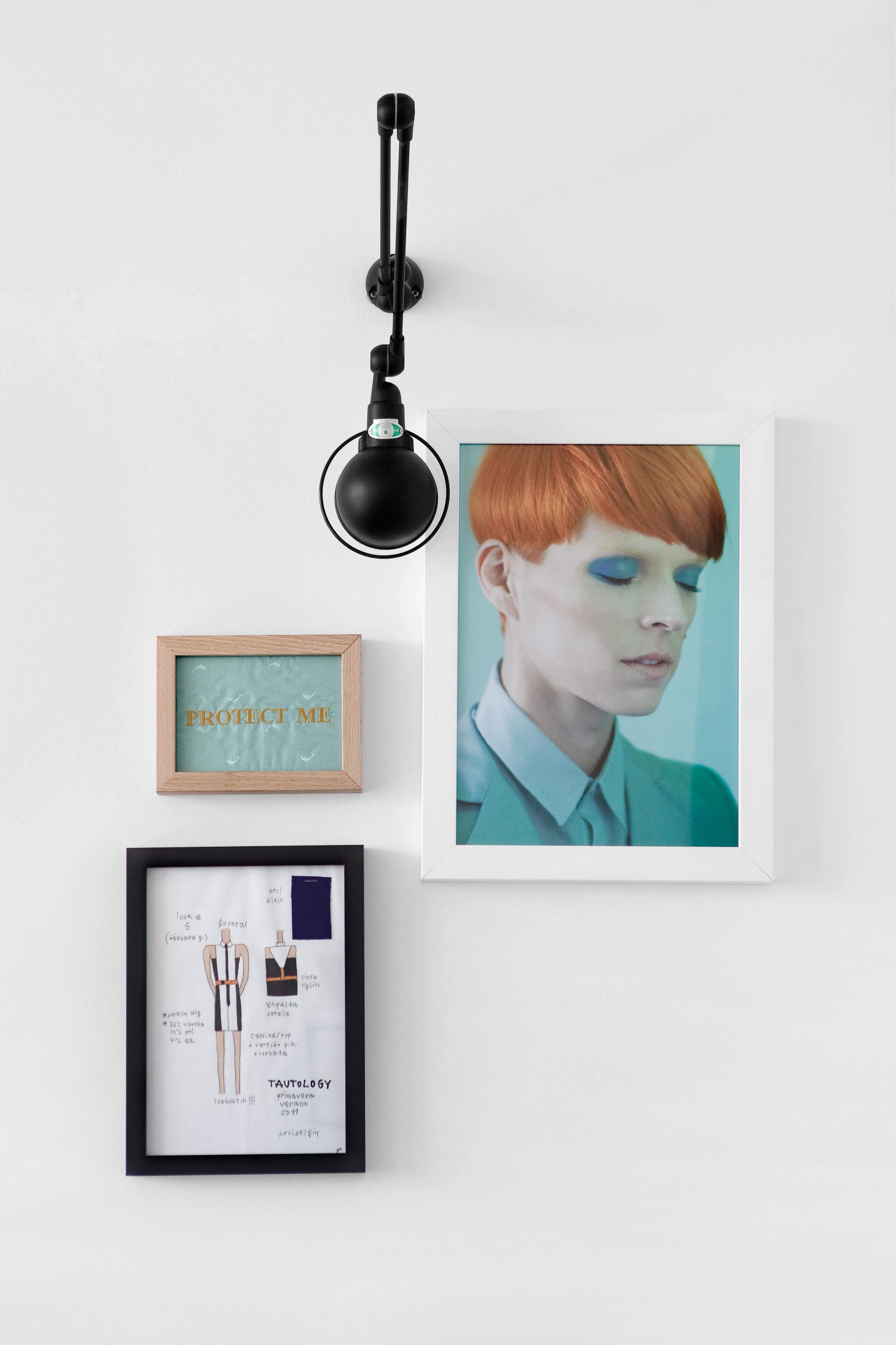 A framed photograph of a person with red hair, a framed artwork with the text "PROTECT ME," and a framed fashion illustration.