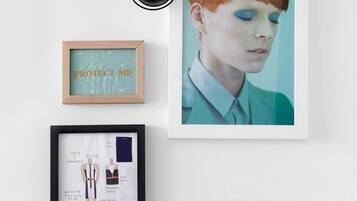 A framed photograph of a person with red hair, a framed artwork with the text "PROTECT ME," and a framed fashion illustration.