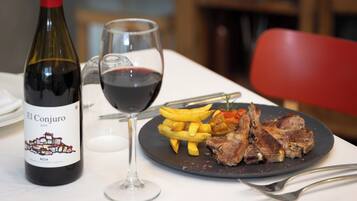Une bouteille de vin El Conjuro, un verre de vin rouge, des frites et de la viande grillée dans une assiette.