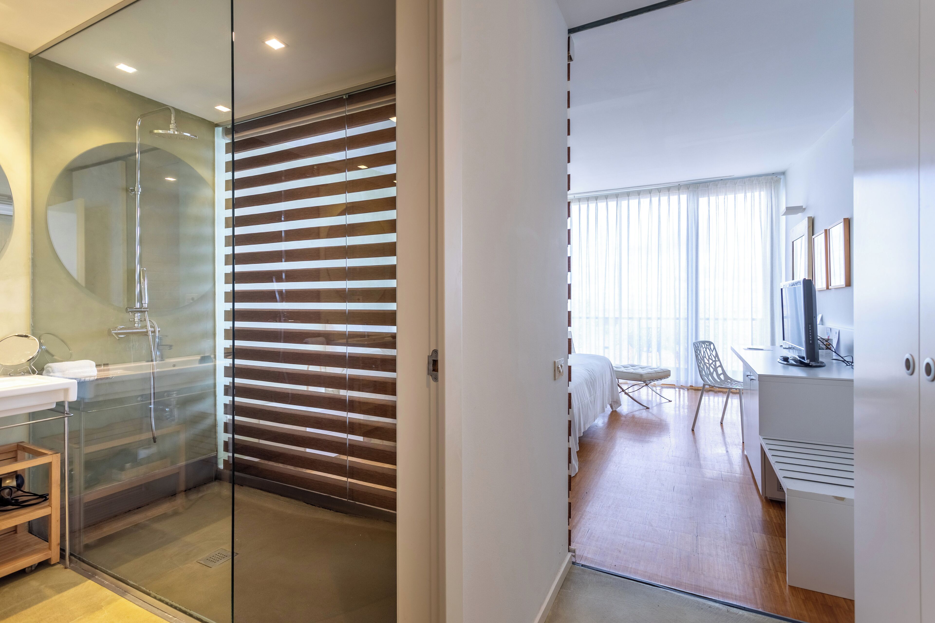 A modern bathroom with a glass shower enclosure, a wooden sliding door, and a white sink with a mirror.