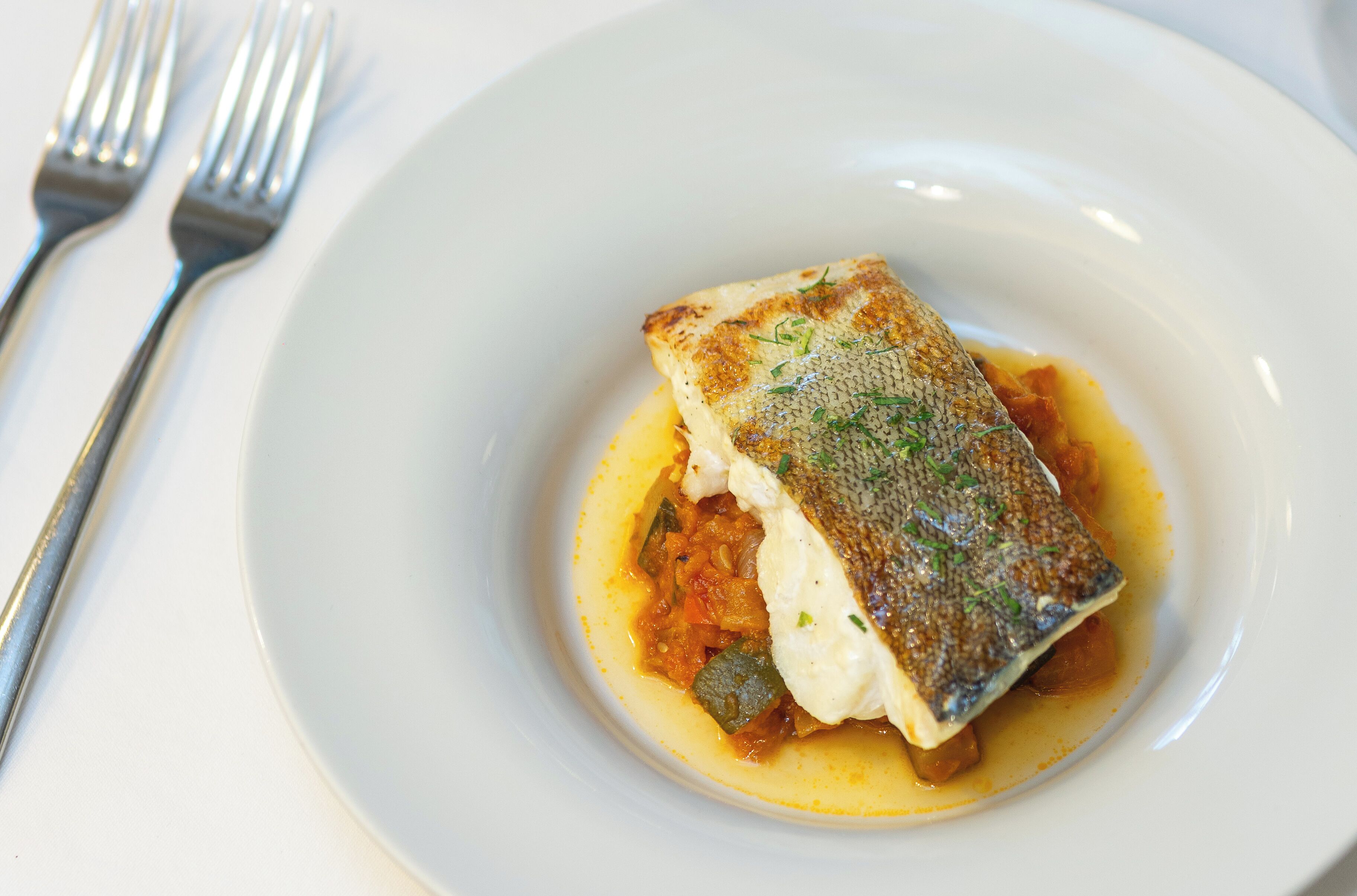 A white plate with a piece of fish and vegetables.