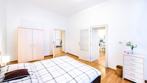 A bedroom with a bed, a wardrobe, and a dresser. There is a hallway leading to a kitchen area.