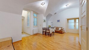 Una habitación amplia con suelo de madera, zona de comedor con sillas y mesa, un sofá y un ventanal grande.