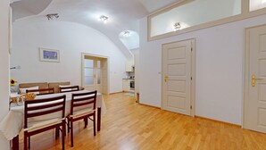 A spacious dining area with a wooden table and chairs, a kitchen in the background, and a high ceiling with recessed lighting.
