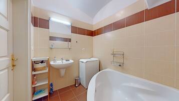 Un baño con un lavabo blanco, un inodoro, una bañera y un estante con artículos de aseo.