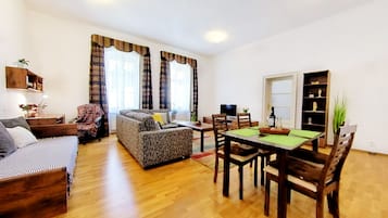 A living room with a sofa, a dining table with chairs, a TV, and a bookshelf.