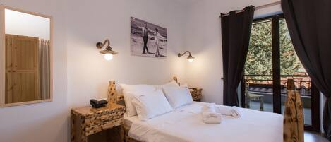 A bedroom with a wooden bed frame, white bedding, a bedside table with a lamp, a mirror, and a picture on the wall.