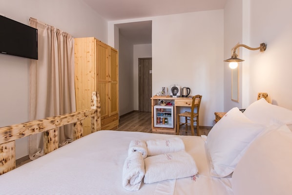 A hotel room with a bed, a wooden wardrobe, a desk with a kettle, and a wall-mounted lamp.