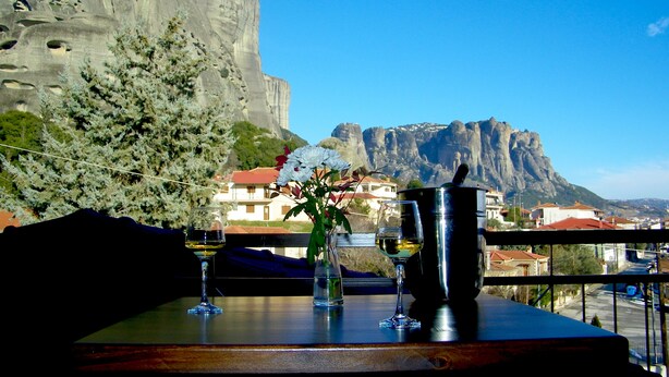 A table with two wine glasses and a vase with flowers, overlooking a mountainous landscape and a town.