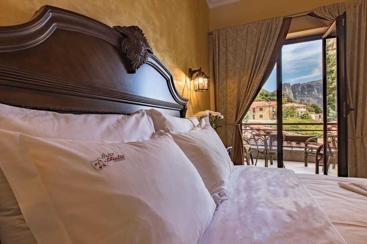 A bedroom with a large bed, a nightstand, a lamp, and a view of the outside.