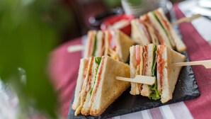 A close-up of a sandwich on a toothpick, placed on a slate board.
