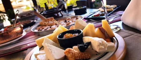 A cheese board with various cheeses, nuts, and a small bowl of fruit on a wooden table.