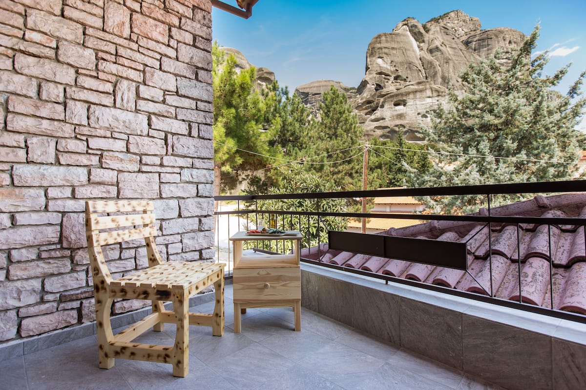 A balcony with a wooden bench and a small table, overlooking a rocky landscape with trees.
