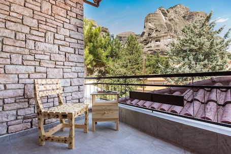 A balcony with a wooden bench and a small table, overlooking a rocky landscape with trees.