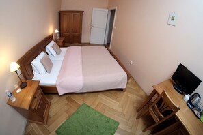 Une chambre d’hôtel bien aménagée, avec un lit, une table de chevet, une lampe, une armoire et un bureau équipé d’une télévision et d’une machine à café.