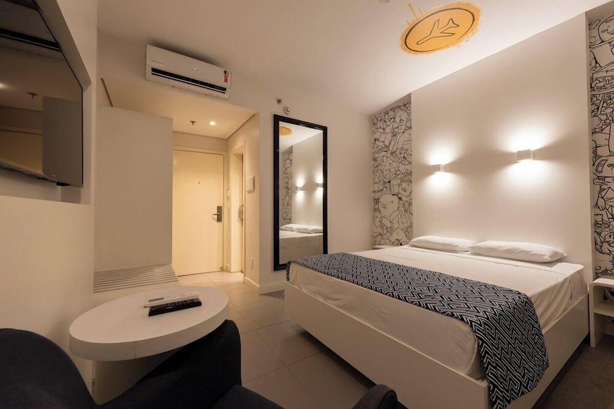 Una habitación de hotel moderna con cama, mesita de noche y espejo.