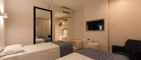 A hotel room with two beds, a TV, a chair, and a wardrobe.