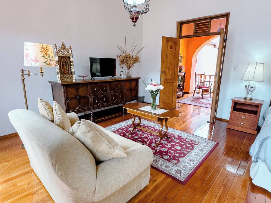Una sala de estar con un sofá, piso de madera, un televisor sobre un mueble, una lámpara decorativa y una puerta que da a otra habitación.
