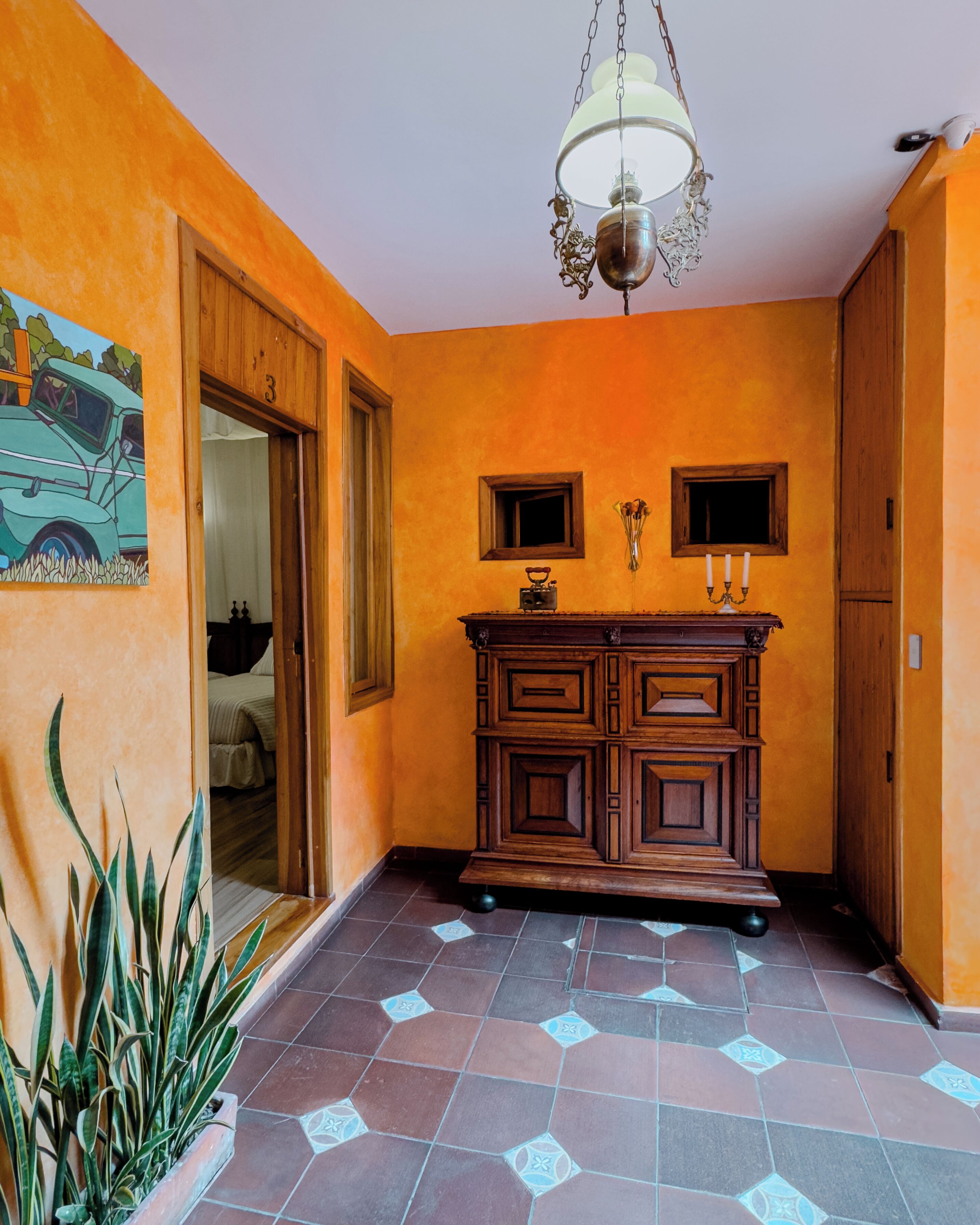 A hallway with orange walls, a wooden cabinet, a tiled floor, and a hanging light fixture.