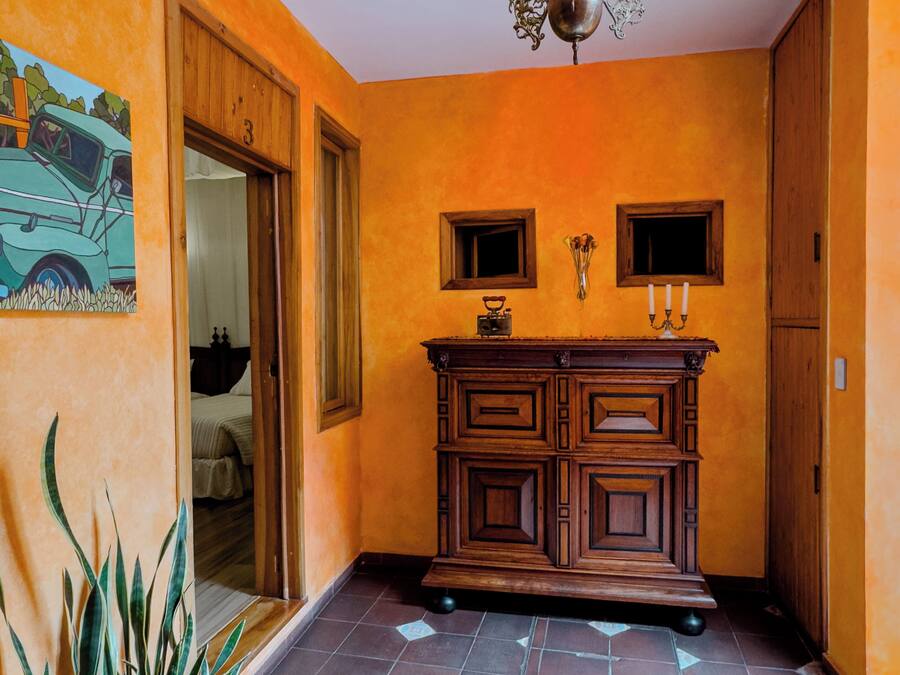 A hallway with orange walls, a wooden cabinet, a tiled floor, and a hanging light fixture.