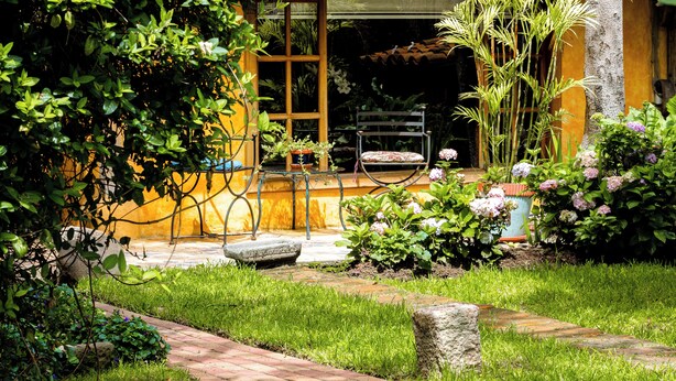 A house with a tiled roof, a wooden door, and a garden with grass, plants, and a pathway. - Hotel Boutique Casa Montalvo Cuenca (Cuenca)